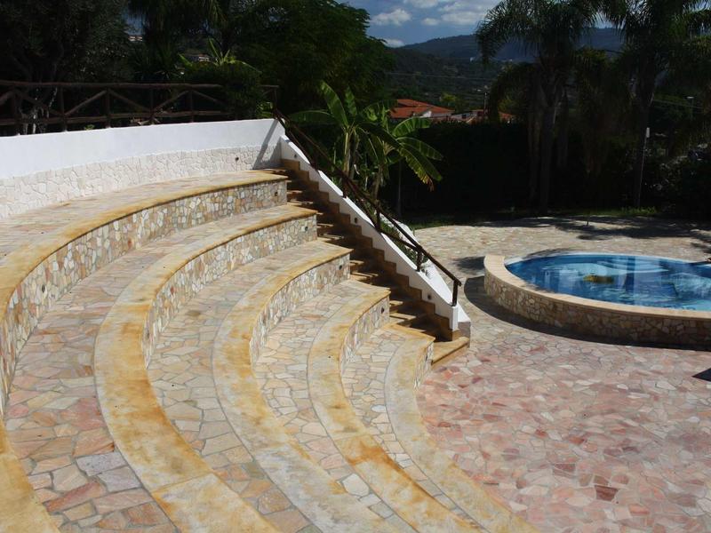 Scala in pietra curva accanto a una piscina rotonda all'aperto con palme.