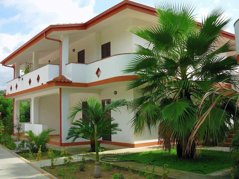 Casa vacanze moderna su due piani con balcone e palme in giardino.