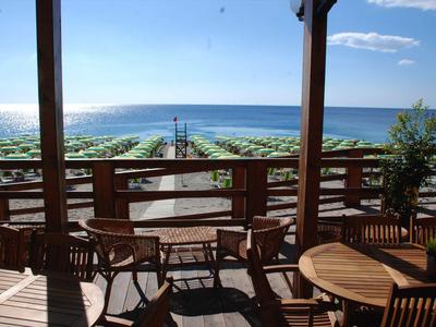 Drewniany taras z stołami i krzesłami z widokiem na plażę z zielonymi parasolami i niebieskim morzem.