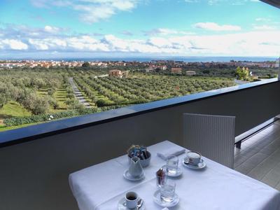 Balkon mit grauem Geländer, weißem Tisch, zwei Tassen und weiter Sicht auf Felder und Stadt.