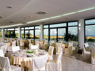 Eleganter Partyraum mit weißen Stühlen, runden Tischen und Panoramafenstern mit Meerblick.