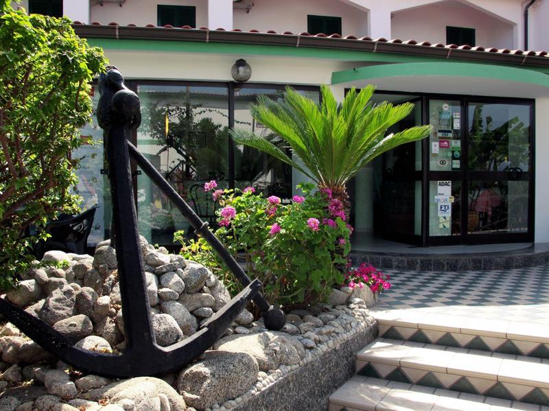 Ancre noire à côté de fleurs et d'escaliers devant un bâtiment blanc avec une bordure de toit verte.