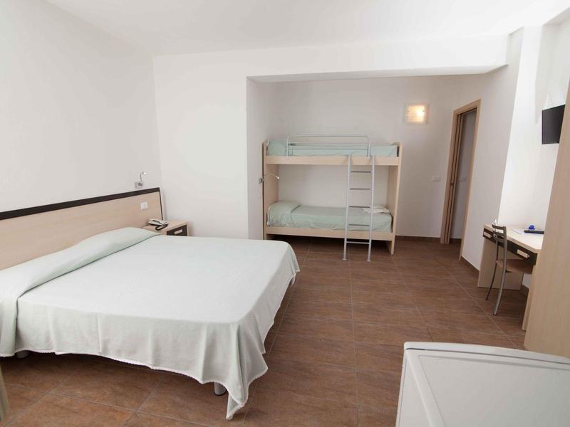 Chambre d'hôtel lumineuse avec grand lit double et lit superposé, mobilier simple.