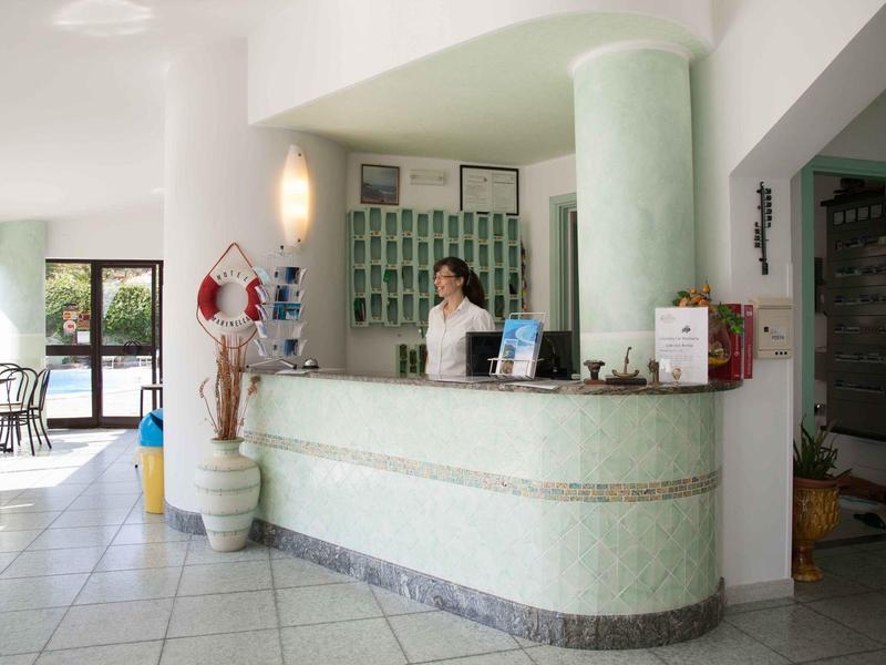 Réception d'hôtel lumineuse avec comptoir, employée et coin salon en arrière-plan.