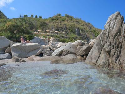 Czysta woda przy skalistej plaży z zielonymi wzgórzami w tle