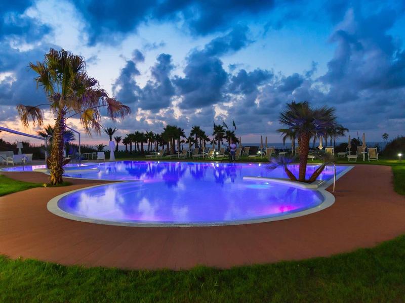 Oświetlony basen otoczony palmami o zmierzchu w kurorcie.