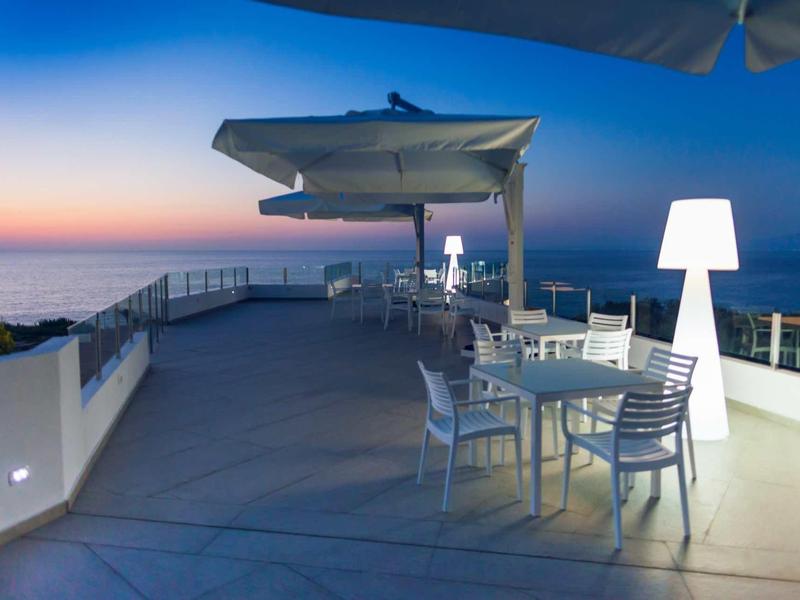 Taras z nowoczesnymi stołami i krzesłami o zachodzie słońca z widokiem na morze w hotelu.