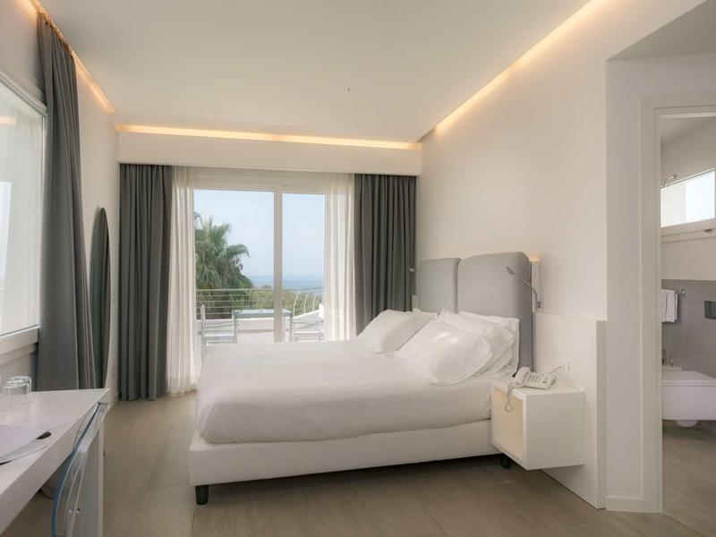 Nowoczesny pokój hotelowy z dużym łóżkiem, oknem z widokiem na morze i przyległą łazienką.