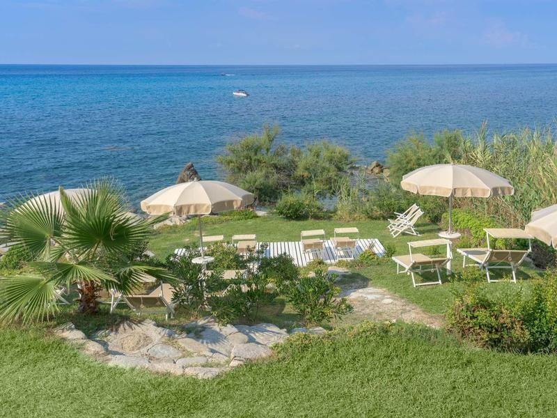 Widok na leżaki i parasole na wybrzeżu z morzem w tle.