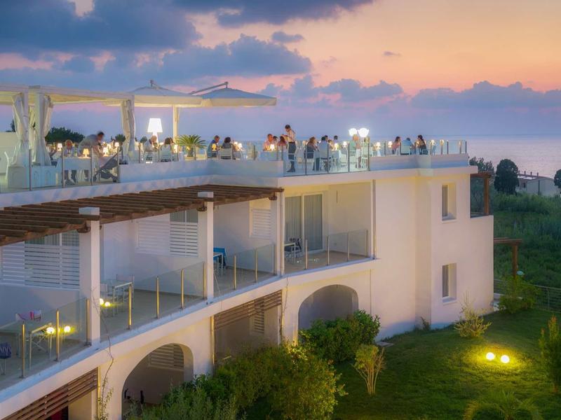 Hotel z oświetlonym basenem i tarasem na zewnątrz o zachodzie słońca z widokiem na morze.
