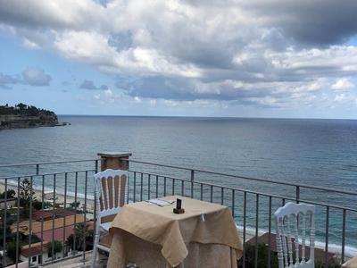 Výhled na moře z terasy se prostřeným stolem a dvěma židlemi pod zataženou oblohou.