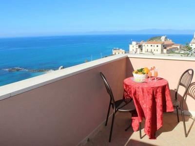 Balcone con piccolo tavolo e sedie, vista sul mare e sugli edifici sullo sfondo.