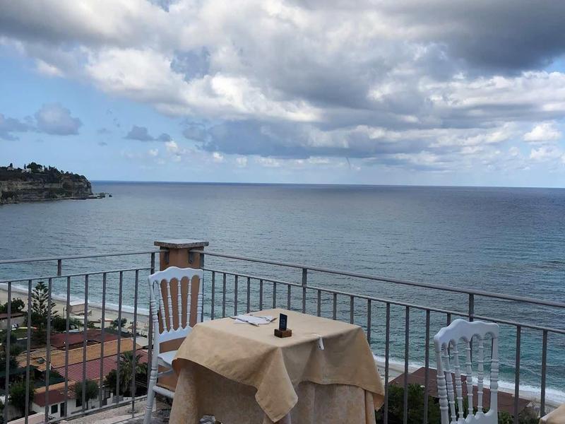 Výhled na moře z terasy se prostřeným stolem a dvěma židlemi pod zataženou oblohou.