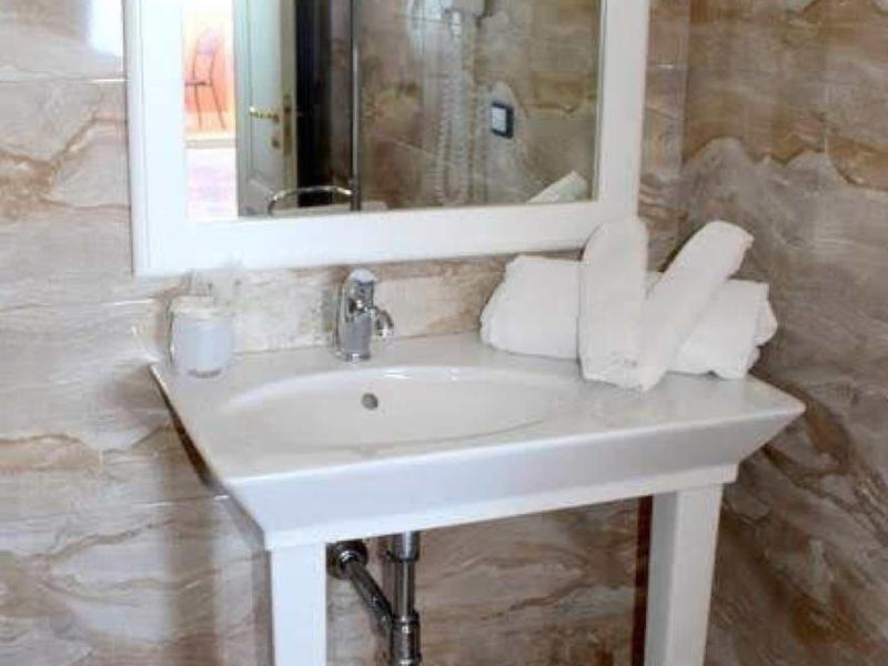 Bílý umyvadlo se zrcadlem a složenými ručníky před béžovými mramorovými stěnami.