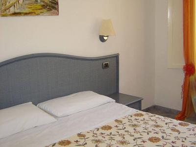 Kleines Schlafzimmer mit blauem Kopfteil, Blumenbettdecke, Nachttisch, Lampe und orangefarbenem Vorhang.