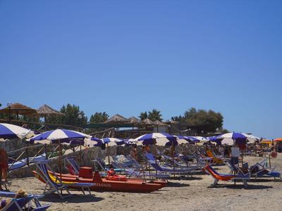 Strand mit Liegestühlen und blauen Sonnenenschirmen unter klarem Himmel.
