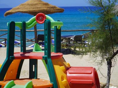 Bunter Kinderspielplatz mit Rutsche am Strand, Meer im Hintergrund, Sonnenschirme und Sand.