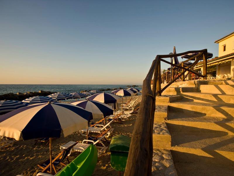Strand mit Sonnenschirmen am Meer, Holzgeländer und Treppe im warmen Abendlicht.