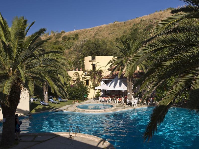 Ein großer blauer Pool mit Palmen und einem Hügel im Hintergrund bei klarem Himmel.