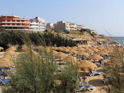 Strand mit Sonnenschirmen und Liegestühlen vor Hotels und Promenade am Meer.