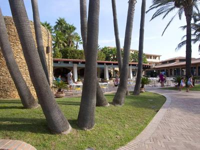 Ein Hotelgebäude mit Palmen im Vordergrund und einem gepflasterten Weg.