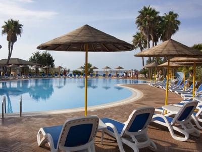 Poolbereich mit Liegestühlen und Sonnenschirmen neben Palmen unter blauem Himmel.