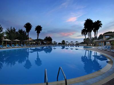 Großer Pool am Abend mit Palmen und Liegestühlen in einem Hotelresort.