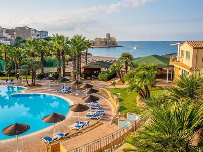 Vista di un resort con piscina, palme, lettini e una fortezza sul mare sullo sfondo.