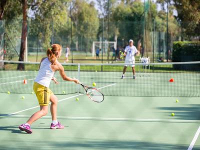 Due persone giocano a tennis su un campo all'aperto con tempo soleggiato.