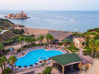 Vista di una piscina dell'hotel accanto a una spiaggia con rocce e mare sullo sfondo.