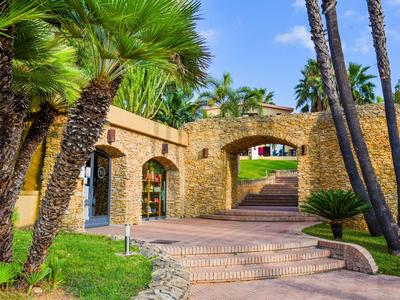 Cortile di un hotel con archi di pietra, palme e percorso lastricato sotto il sole.