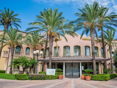 Hotel in stile mediterraneo circondato da palme sotto un cielo azzurro limpido.