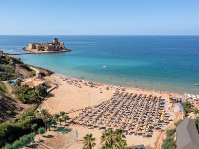 Spiaggia di sabbia con lettini e ombrelloni vicino a rovine sul mare azzurro chiaro.