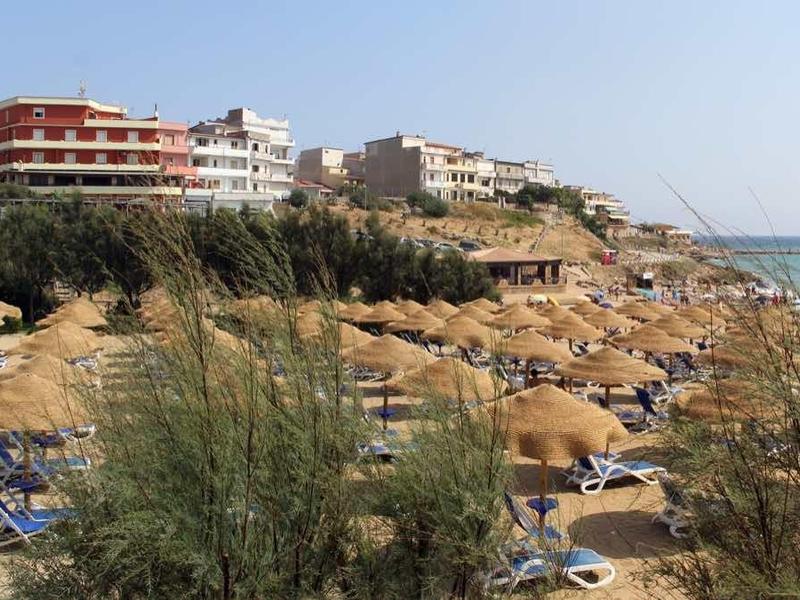 Strand mit Sonnenschirmen und Liegen, dahinter Felsen, Gebäude und ein Schloss am Meer.