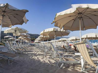 Strand met ligstoelen en parasols onder een heldere blauwe lucht op een vakantiebestemming.