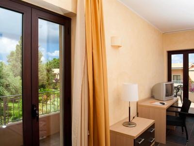 Lichte hotelkamer met balkon, gele gordijnen en licht houten meubels.