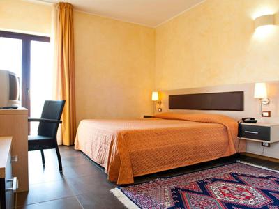 Eenvoudig ingericht hotelkamer met tweepersoonsbed, tv en tapijt op een donkere vloer.