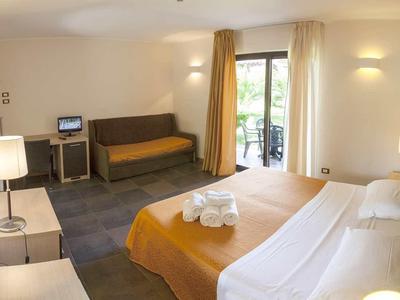 Hotelkamer met tweepersoonsbed, bank, bureau en balkon met uitzicht op groen.