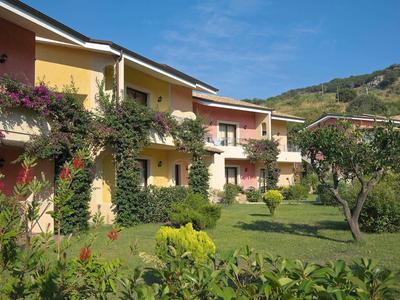 Bunte Ferienwohnungen mit Garten, Bäumen und Hügeln im Hintergrund an einem sonnigen Tag.