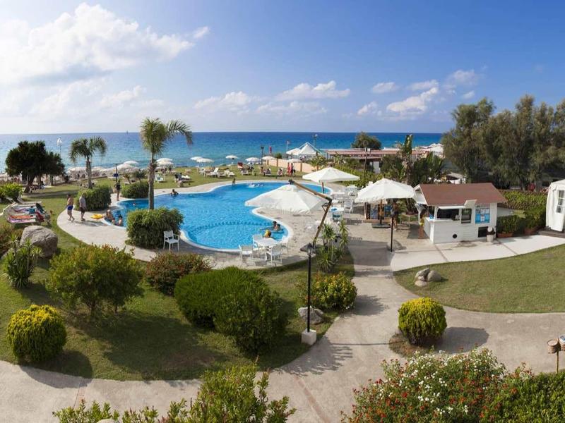 Uitzicht op een buitenzwembad met ligstoelen, paviljoenen en een verzorgde tuin met zeezicht.