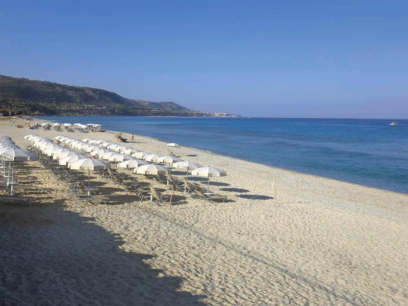 Leeg zandstrand met rijen witte parasols en blauwe zee onder een heldere lucht.