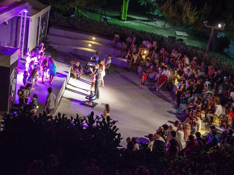 Buitenpodium 's nachts met een band die optreedt en publiek in een openluchttheater.