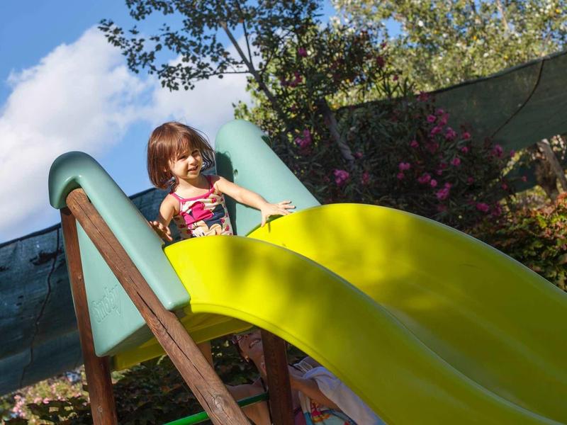 Een kind glijdt naar beneden van een gele glijbaan op een zonnige dag buiten.