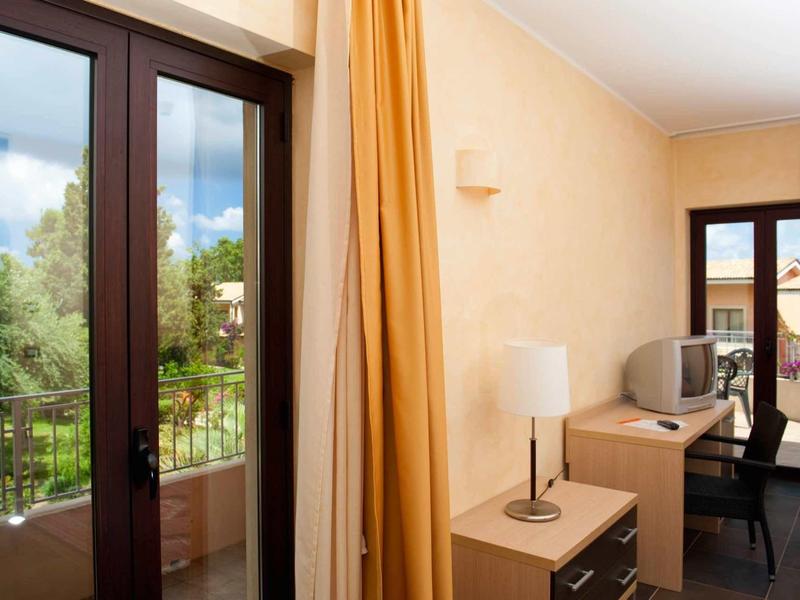 Lichte hotelkamer met balkon, gele gordijnen en licht houten meubels.