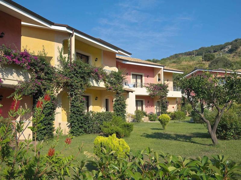 Verschillende tweeverdiepings vakantiehuizen met kleurrijke gevels en verzorgde tuin onder blauwe lucht.