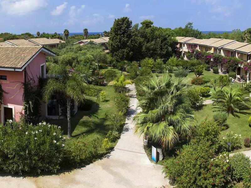 Hotelcomplex met Mediterrane gebouwen, weelderige tuinen en stenen paden onder een blauwe lucht.