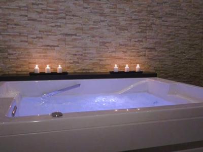 Vírivá vana s modře osvětlenou vodou a svíčkami před kamennou zdí.