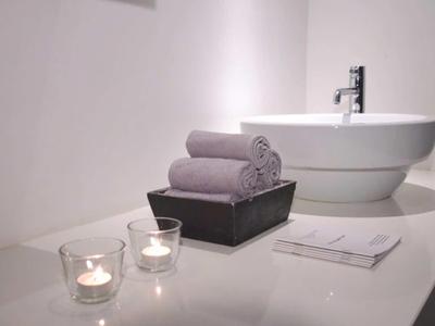 Moderní koupelnové zařízení s kulatým umyvadlem, ručníky a svíčkami na bílé ploše.