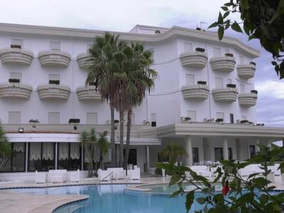 Hotelgebäude mit mehreren Balkonen und Pool im Vordergrund, Palmen umgeben das Areal.