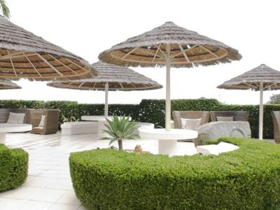 Große Terrasse mit grünen Hecken, weißen Sitzgruppen und Strohhut-Sonnenschirmen.